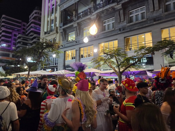 Multitud disfrazada celebrando el carnaval de noche en una calle animada de Santa Cruz, rodeada de edificios iluminados y ambiente festivo.