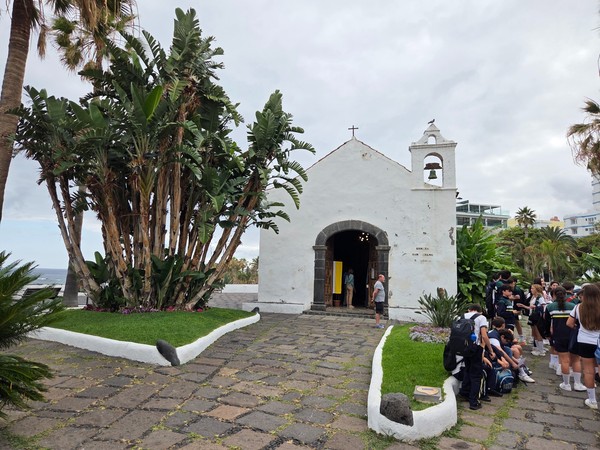 Ermita junto al mar Pequeña ermita blanca junto al mar con palmeras y visitantes en un entorno tranquilo y tradicional.