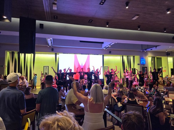 Música en Hard Rock Cafe Actuación musical en el interior de Hard Rock Cafe, con varios artistas sobre el escenario y el público participando con los brazos levantados.
