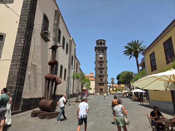 Calle histórica de La Laguna con la torre de la iglesia al fondo, palmera y edificios tradicionales canarios.