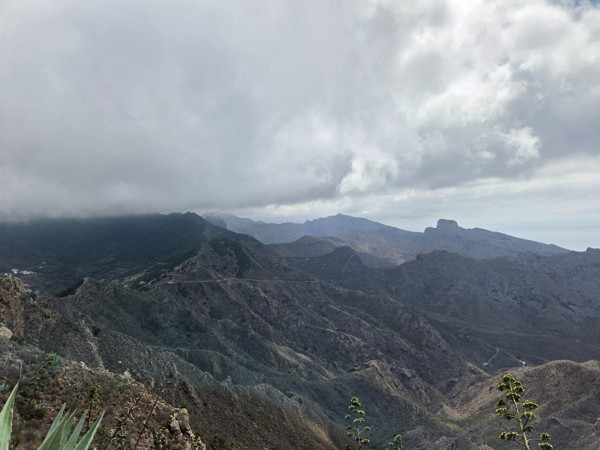 Montañas bajo las nubes Paisaje montañoso y volcánico de Tenerife bajo un cielo cubierto, con crestas escarpadas y una carretera que cruza la ladera.