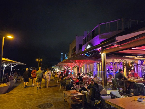 Noche en Playa de las Américas Paseo nocturno en Playa de las Américas con terrazas iluminadas, personas caminando junto al mar y ambiente animado en la zona de restaurantes.