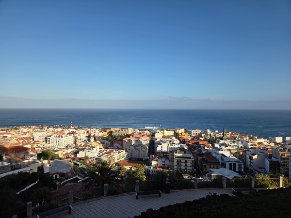 Vista de Puerto de la Cruz Vista elevada de Puerto de la Cruz con tejados, edificios y el océano Atlántico extendiéndose en el horizonte.