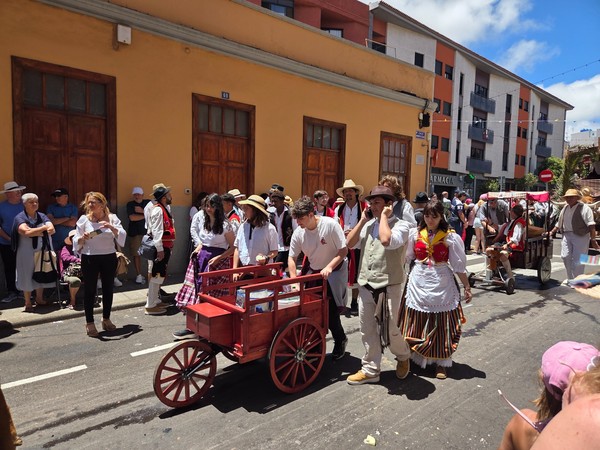 Desfile tradicional en la calle Desfile festivo en una calle con personas vestidas con trajes tradicionales y carretas de madera durante una celebración popular.